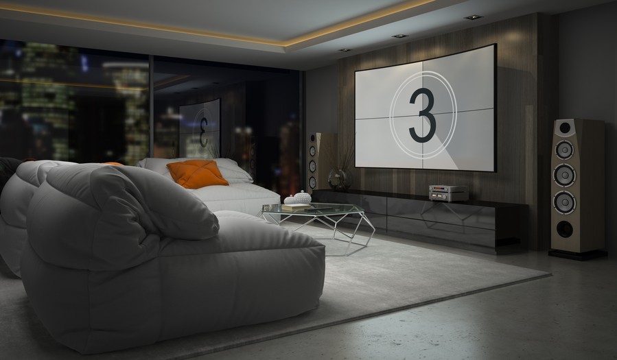 A home theater with a widescreen display, floor-standing speakers, and gray couches. 