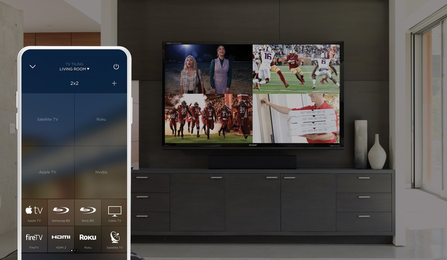 A living room setup showcasing a smart TV with Savant's video tiling feature displaying four different video sources. A smartphone app is shown in the foreground 