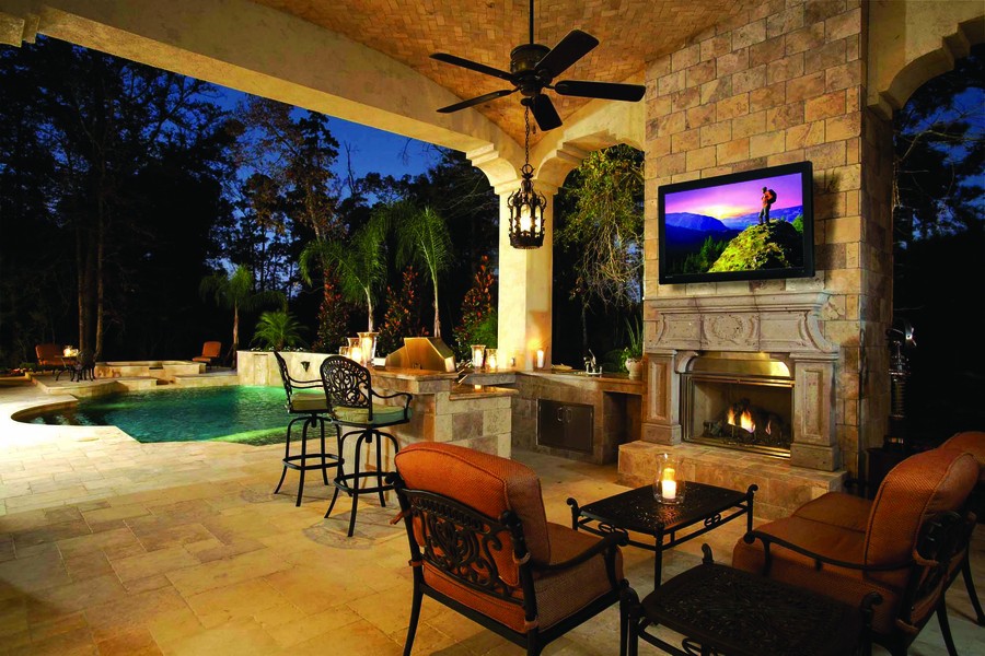 A backyard with a pool and a patio with a fireplace, pendant light, and candlelight.